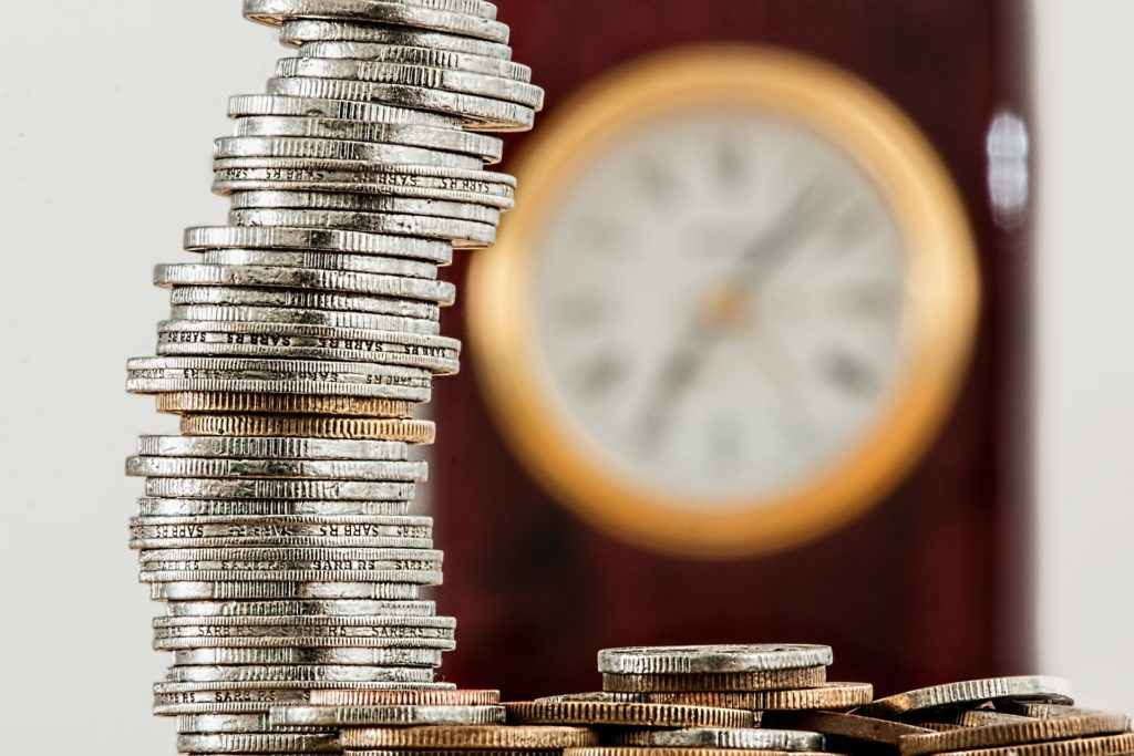 silver and gold coins in front of a wall clock