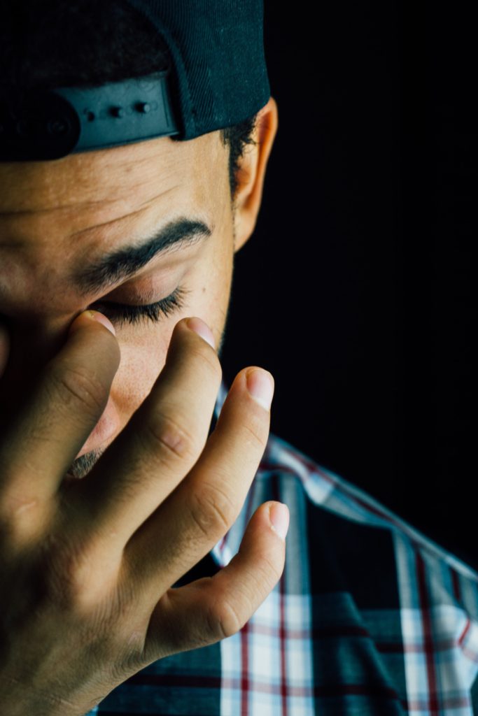 man with eyes closed pinching bridge of nose with thumb and forefinger