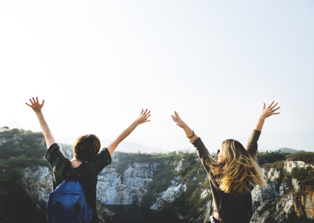 two people with their hands in the air while facing a sunny gorge