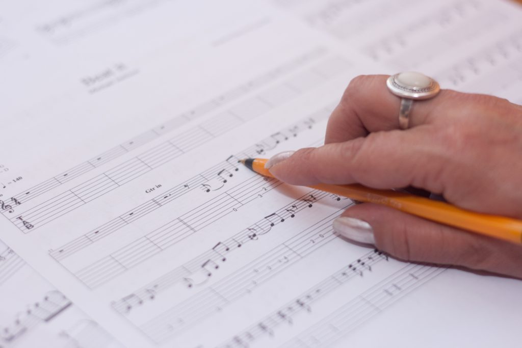 hand holding a pencil over a page of sheet music