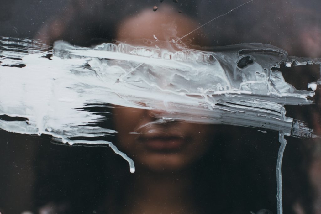 woman looking through glass with paint over face