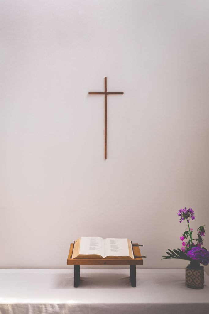 bible and flower on table under a cross